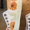 White high-top sneaker with orange sunflower print on the side, placed on a wooden surface.