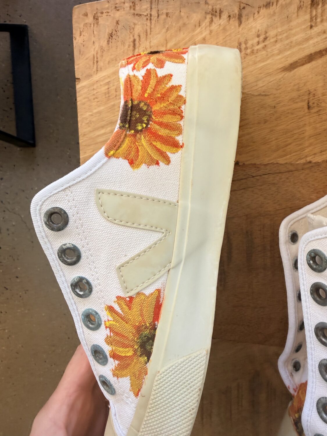 White high-top sneaker with orange sunflower print on the side, placed on a wooden surface.