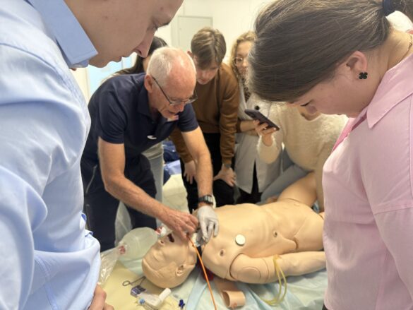 Medical training scene: a group of students and an instructor rehearsing airway management on a life-size manikin.