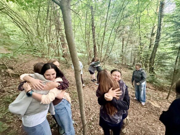 IMG_6410 Group of people hugging on a forest path among trees and fallen leaves, enjoying a moment together during a outdoor gathering.