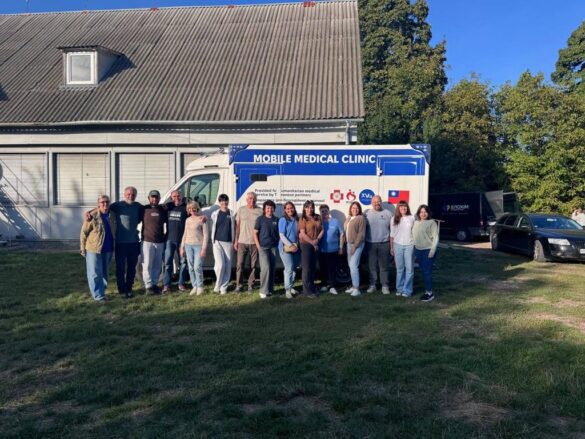 Group of people standing in front of a blue and white Mobile Medical Clinic van outdoors on a grassy area.