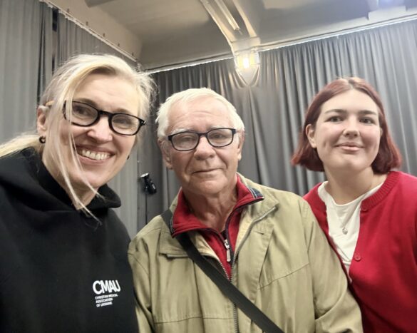 Three people posing for a selfie indoors: a smiling woman with glasses on the left, an older man with glasses in the middle, and a young woman with red hair on the right.