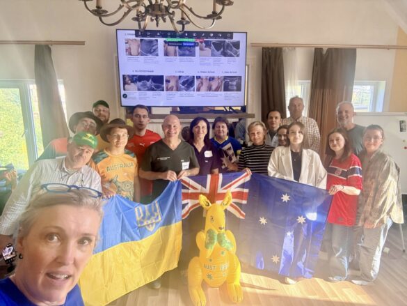 Group of adults indoors posing with Ukrainian and Australian flags; a yellow inflatable kangaroo stands in front, with a screen on the wall behind them.