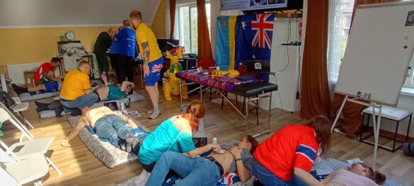 People on mats receive hands-on medical training in a sunny room, with instructors guiding chest compressions and care.