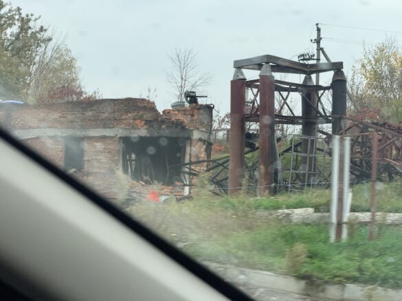 IMG_8866 Ruined brick building with collapsed roof and rusted metal framework seen from a car window by the road